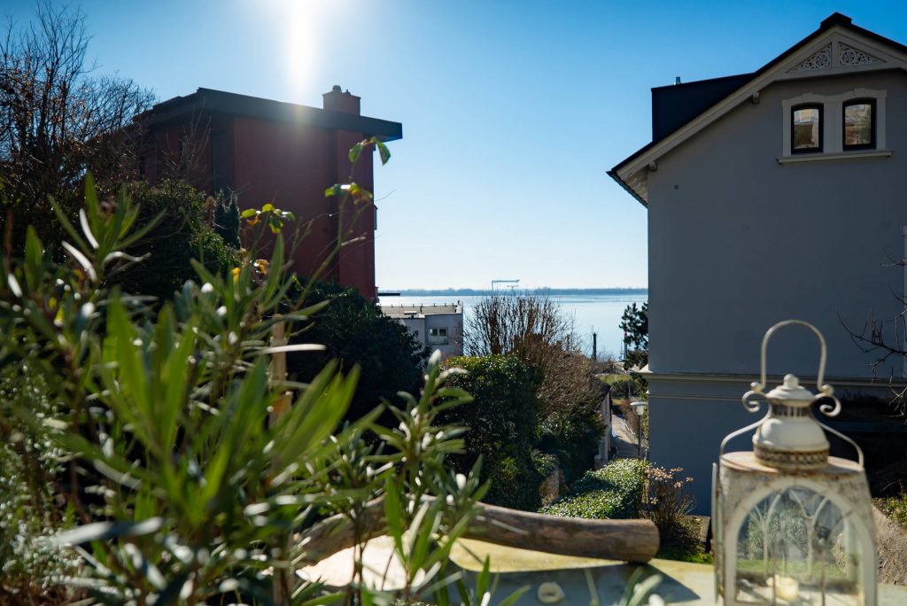 Immobilienfotografie Treppenviertel Hamburg Blankenese, Block von Balkon zwischen benachbarten Häusern hindurch auf die Elbe bei strahlend blauem Himmel.