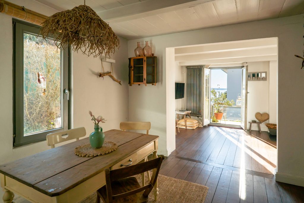 Immobilienfotografie Hamburg Blankenese, Blick aus dem Esszimmer durch das Wohnzimmer auf die geöffnete Balkontür mit Sonnenschein von außen.