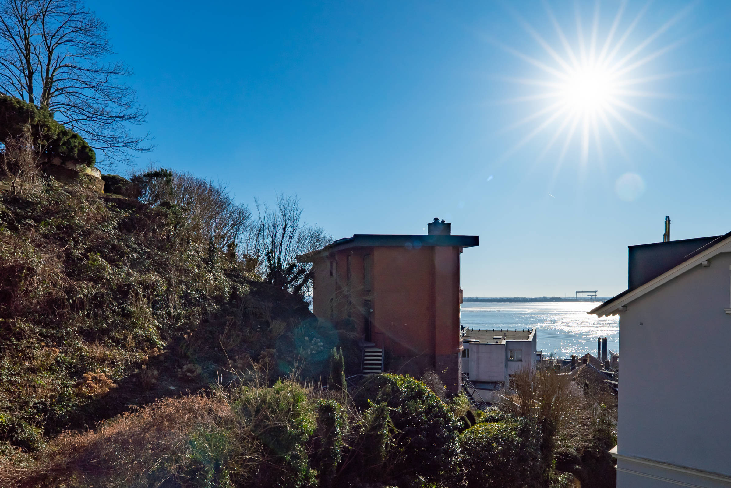 Blick von einer Immobilie im Treppenviertel Blankenese aus auf die Elbe bei blauem Himmel und Sonnenschein.